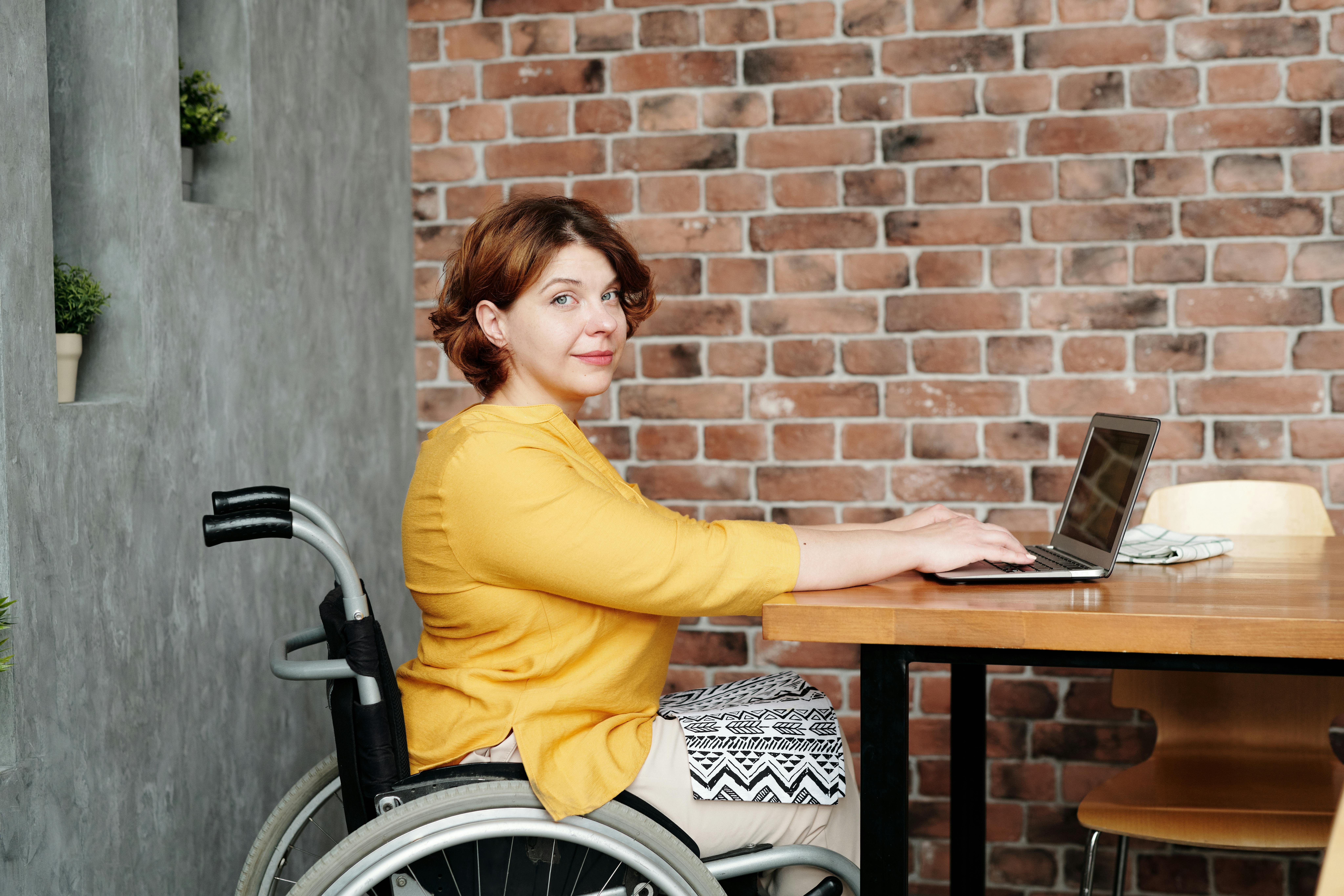A woman in a wheelchair working remotely on a laptop in a cozy home environment.